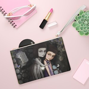 May include: A white zippered pouch with a black and white illustration of two girls holding hands. The girls are wearing dresses and have dark hair. The background is a dark forest scene with butterflies and a book.