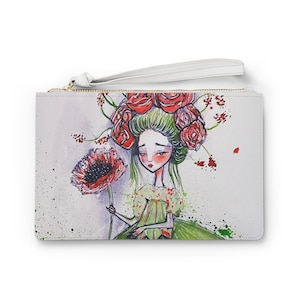 Op de afbeelding: Een witte clutch met een ritssluiting en een witte band. De voorkant van de clutch heeft een aquarel-illustratie van een meisje met rode bloemen in haar haar en een groene jurk die een rode klaproos vasthoudt.
