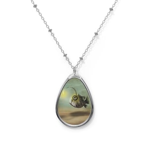 May include: A silver chain necklace with a teardrop-shaped pendant featuring a black and white illustration of a deep-sea anglerfish with a glowing lure.