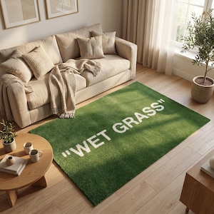Peut inclure: Un tapis rectangulaire présentant une texture vert vif rappelant l'herbe, avec le texte "WET GRASS" imprimé en grandes lettres capitales blanches et grasses au centre. Le tapis possède une surface à poils courts et denses.