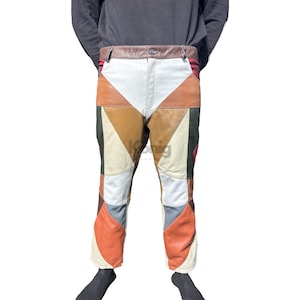 Op de afbeelding: Veelkleurige leren broek met een patchwork-ontwerp. De broek heeft een verscheidenheid aan geometrische vormen in tinten wit, bruin, oranje, groen en grijs. De tailleband is van bruin leer en de broek heeft een knoopsluiting.
