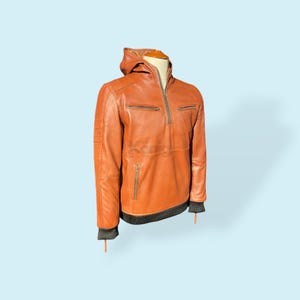 Puede incluir: Una chaqueta de cuero marrón con capucha y cierre de cremallera. La chaqueta tiene un ribete de punto de canalé en los puños y el dobladillo.