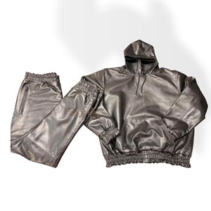 May include: A dark brown faux leather matching set consisting of a hooded sweatshirt and trousers. The hoodie features a front kangaroo pocket, drawstring hood, and gathered elastic cuffs and hem. The trousers have a side zipper pocket.