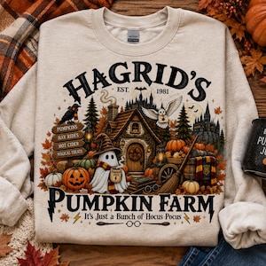 May include: A beige crewneck sweatshirt featuring a graphic print with the text HAGRID'S EST. 1981 PUMPKIN FARM and It's Just a Bunch of Hocus Pocus. The design includes a ghost, a cottage, a broom, pumpkins, an owl, and a sign listing fall activities.