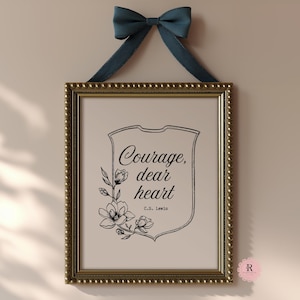 May include: A framed print with the quote "Courage, dear heart" by C.S. Lewis. The print is in a gold frame and is adorned with a navy blue bow. The artwork features a floral design and is suitable for home decor.