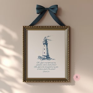 May include: Framed print featuring a blue and white lighthouse illustration. The artwork includes the text "The Lord is my light and my salvation..." from Psalm 27:1. The print is in a gold frame and is suspended by a navy blue ribbon.