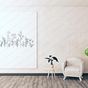 May include: A white wall with a framed black and white line drawing of a row of flowers. A white armchair sits in front of the wall, and a small table with a green plant sits to the left of the chair.