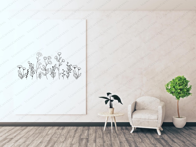May include: A white wall with a framed black and white line drawing of a row of flowers. A white armchair sits in front of the wall, and a small table with a green plant sits to the left of the chair.