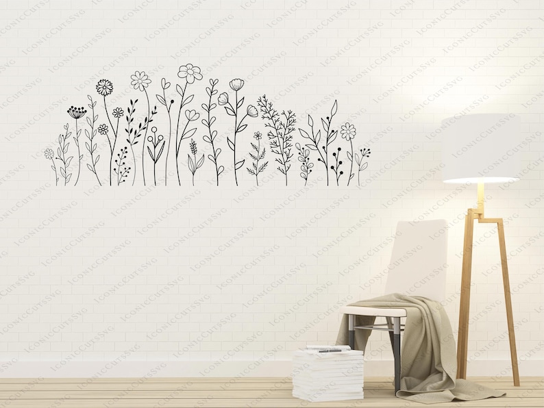 May include: A black and white line drawing of a row of stylized flowers and plants on a white wall. A white chair with a brown throw blanket is in the foreground, and a floor lamp with a white shade is to the right of the chair.