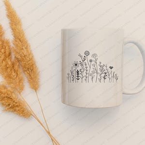 May include: White ceramic mug with a black line drawing of a row of wildflowers. The mug has a handle on the right side.