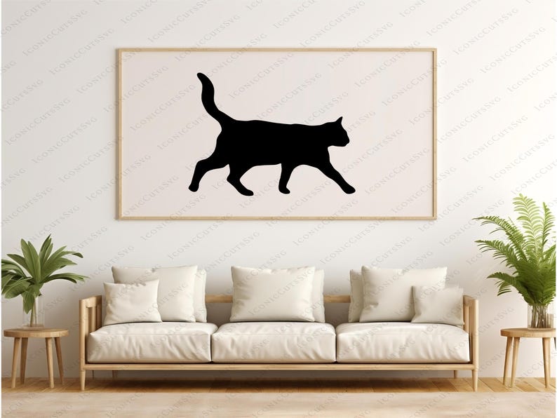 May include: A black cat silhouette in a walking pose is printed on a white background in a framed picture hanging on a white wall. A white sofa with cushions is in the foreground.