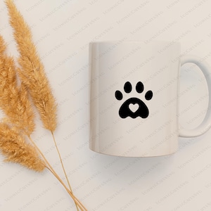 May include: White ceramic mug with a black paw print design featuring a small heart in the centre. The mug has a handle and is on a white background.