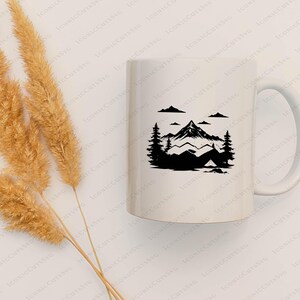 May include: White ceramic mug featuring a black mountain and camping scene. The design includes a mountain range, trees, clouds, and a tent. The mug has a curved handle and is suitable for hot or cold beverages.
