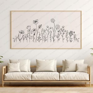 May include: A black and white line art print of a floral arrangement with various types of flowers and leaves. The print is framed and hanging on a white wall above a white couch.