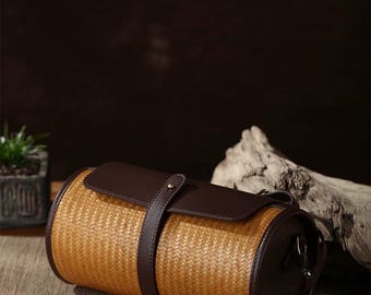 May include: A brown leather and woven cylindrical bag with a strap. The bag has a brown leather flap with a buckle.