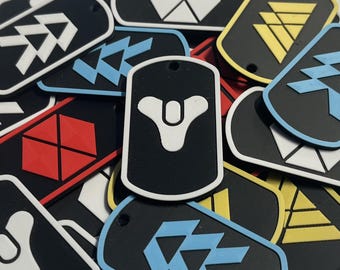 May include: A collection of rectangular dog tags featuring various geometric symbols in white, blue, red, and yellow on black backgrounds. Each tag has a small hole at the top for attachment, with a prominent white Destiny logo emblem centered.
