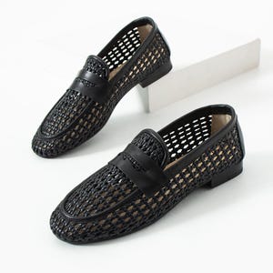 May include: A pair of black woven leather loafers with a classic penny strap design. The shoes have a low heel and a breathable, open weave pattern. The loafers are displayed on a white surface.