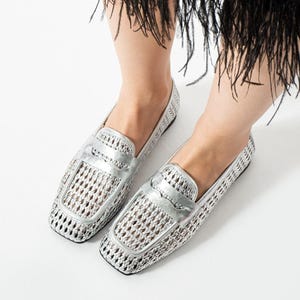 Puede incluir: Mocasines plateados tejidos con punta cuadrada y detalle de correa metálica. Los zapatos tienen un diseño de tejido abierto y un tacón bajo. Estos elegantes zapatos sin cordones son una opción de moda para uso casual.