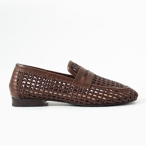 May include: Brown woven leather loafer with a classic design. The shoe features a woven pattern across the vamp and sides, with a solid leather trim and a small heel. A leather strap detail is across the top.