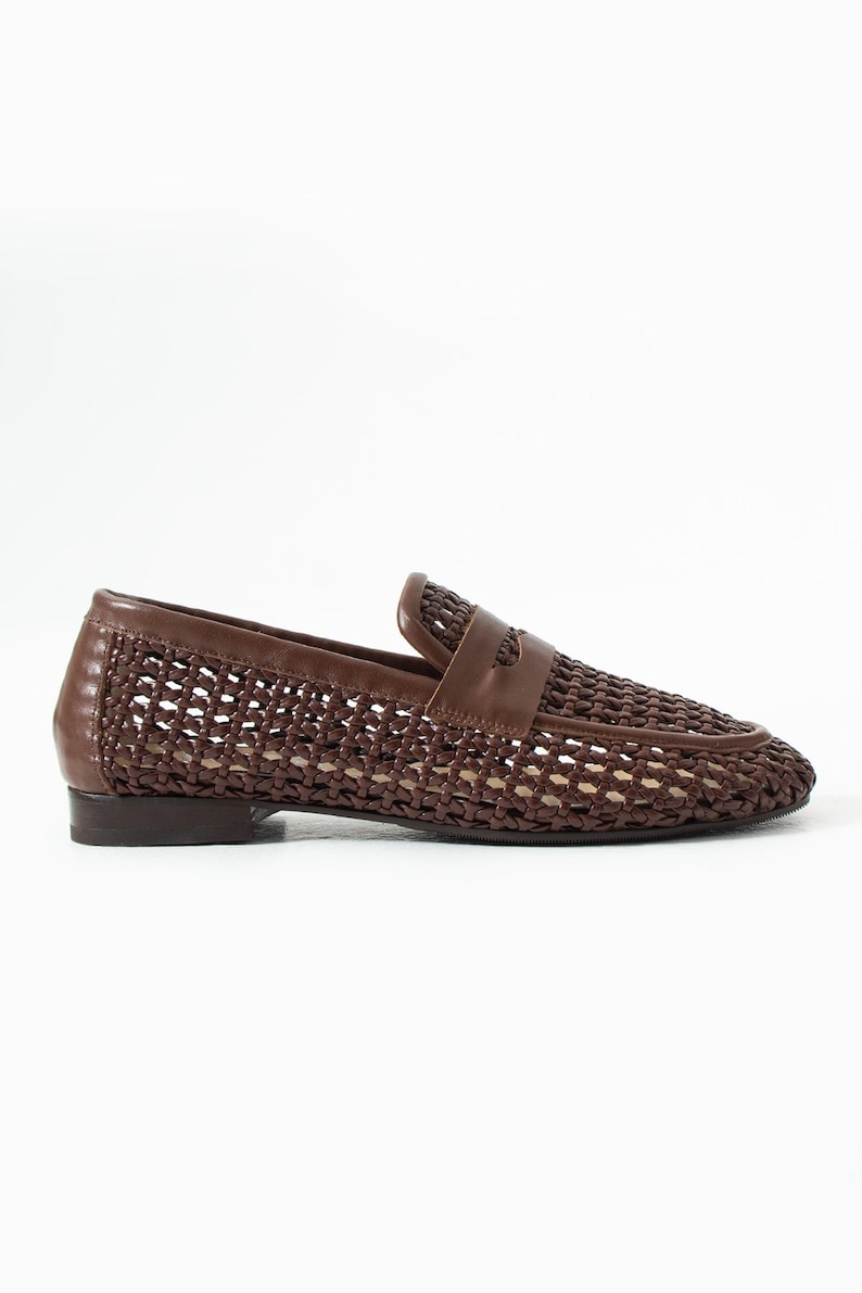 May include: Brown woven leather loafer with a classic design. The shoe features a woven pattern across the vamp and sides, with a solid leather trim and a small heel. A leather strap detail is across the top.