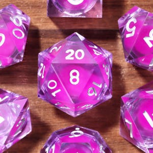 May include: Set of seven clear, faceted dice with a vibrant pink core and white numbering. The dice are in various geometric shapes, including a cube, a d20, and a d6, perfect for tabletop gaming.