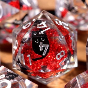 May include: A collection of clear, multi-sided dice with a red glitter interior and black cat illustrations. The dice feature white numbers and are designed for tabletop gaming. The dice are in various shapes and sizes.