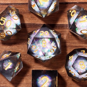 May include: Set of seven clear, multi-faceted dice with gold-colored numbers. Each die has a shimmering, iridescent core. The dice are arranged on a wooden surface, showcasing their geometric shapes and reflective qualities. Ideal for tabletop gaming.