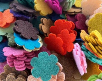 May include: A pile of colorful felt flower shapes in various colors, including red, pink, purple, green, yellow, and brown. The felt flowers are stacked and scattered, creating a vibrant and textured display. These are ideal for crafting and DIY projects.