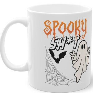 May include: White ceramic coffee mug with a black and white ghost, a black bat, and a spider web design. The text "Spooky Sh*t" is printed in orange and black.