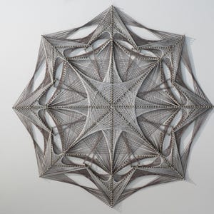 May include: A white and brown string art piece in the shape of a starburst. The piece is made with string wrapped around nails hammered into a wooden board.