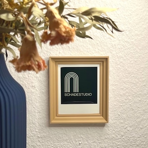 Könnte beinhalten: Ein gerahmter Druck mit schwarzem Hintergrund und einem weißen abstrakten Design eines Bogens. Der Text "SCHADESTUDIO" ist unter dem Design gedruckt.
