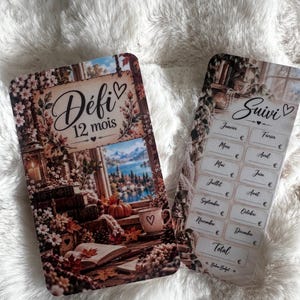 May include: Two rectangular paper trackers with a cosy autumn theme. The left card features the text Défi 12 mois, a window view, books, and a pumpkin. The right card features the text Suivi, a list of twelve months from Janvier to Décembre with blank spaces for currency amounts, and the text Total.