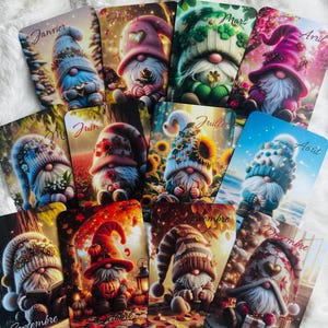 Peut inclure: Un ensemble de douze cartes, chacune représentant un gnome illustré pour un mois de l'année. Les gnomes portent des chapeaux colorés et sont placés sur des scènes saisonnières. Chaque carte affiche le nom du mois en français.