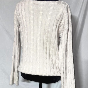 May include: A cream-colored cable knit sweater with a navy blue and white striped collar.