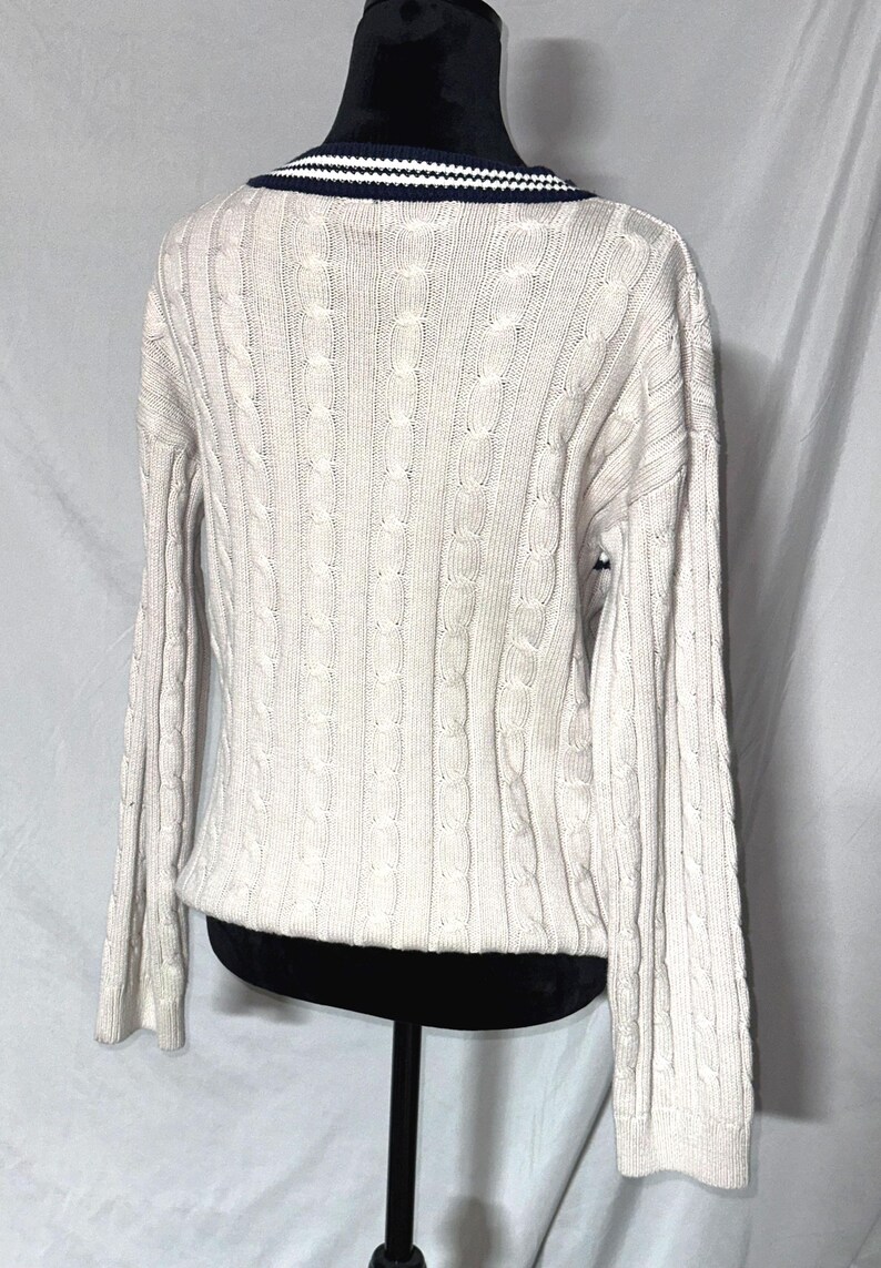 May include: A cream-colored cable knit sweater with a navy blue and white striped collar.