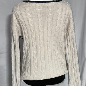 May include: A cream colored cable knit sweater with a navy blue and white striped collar.