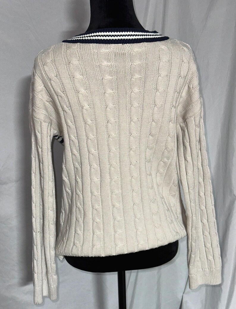 May include: A cream colored cable knit sweater with a navy blue and white striped collar.