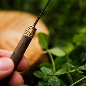 Puede incluir: Una herramienta delgada con un mango de madera marr&oacute;n oscuro y una punta de metal fina y afilada. Una virola de metal color lat&oacute;n conecta el mango con la punta, mostrando un peque&ntilde;o emblema circular en relieve de una cabeza de carnero.