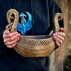 May include: A wooden Viking ship bowl, hand-carved with detailed scrollwork and geometric patterns. The bowl's curved design and natural wood grain give it a rustic appearance. The bowl is a decorative item, perfect for display or as a unique serving piece.