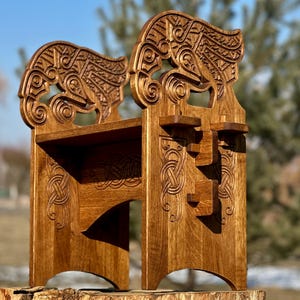 Op de afbeelding: Een houten stoel met ingewikkelde houtsnijwerk in de vorm van een drakenkop. De stoel is donkerbruin gebeitst en heeft een plank aan de achterkant.