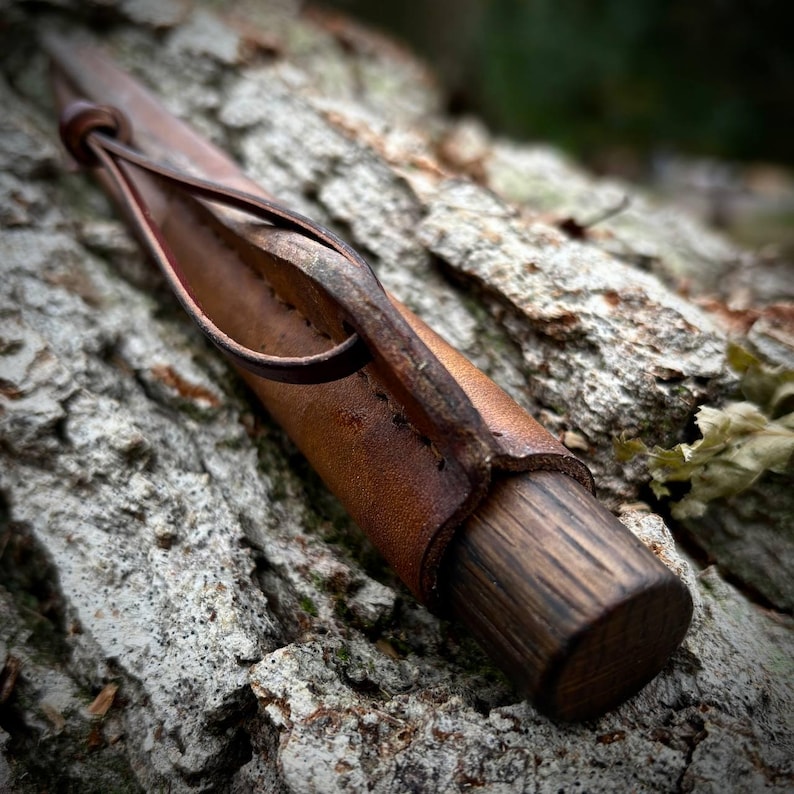 Puede incluir: Una funda de cuero marr&oacute;n con una costura cosida y un lazo para un cintur&oacute;n. La funda est&aacute; envuelta alrededor de un mango de madera.