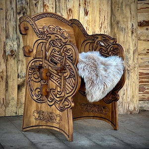 Op de afbeelding: Een houten stoel met ingewikkelde houtsnijwerk van Keltische knopen en draken. De stoel heeft een hoge rugleuning en een dikke, gepolsterde zitting. De stoel is gemaakt van donker hout en heeft een rustieke, antieke uitstraling.