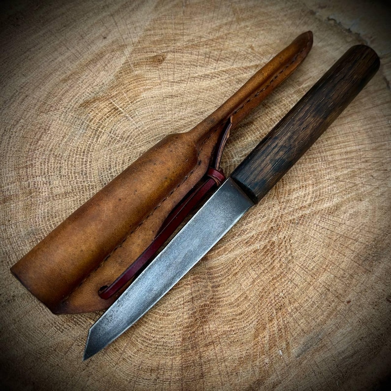 Puede incluir: Un cuchillo hecho a mano con mango de madera oscura y una funda de cuero. La hoja est&aacute; hecha de acero y tiene una punta afilada.