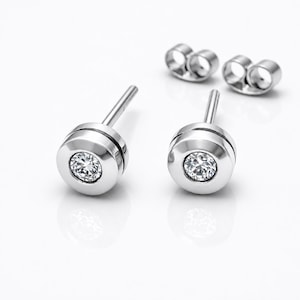 May include: A pair of silver-toned stud earrings featuring a circular bezel setting with a single clear, faceted round gemstone in the center. Each earring includes a post back and a separate matching silver-toned butterfly earring back.