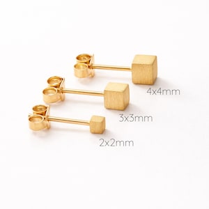 May include: Three gold-colored square stud earrings in varying sizes: 2x2mm, 3x3mm, and 4x4mm. Each earring features a post and a small, square cube design. The earrings are displayed on a white background.