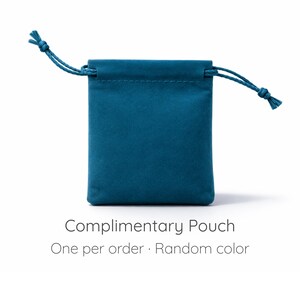 May include: A teal drawstring pouch with a soft, matte texture. The pouch features two matching teal cords with knotted ends for closure. Below the pouch, the text reads: Complimentary Pouch. One per order &middot; Random color.