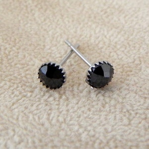 May include: A pair of black stud earrings with a silver setting. The earrings have a round, faceted black stone in the center.