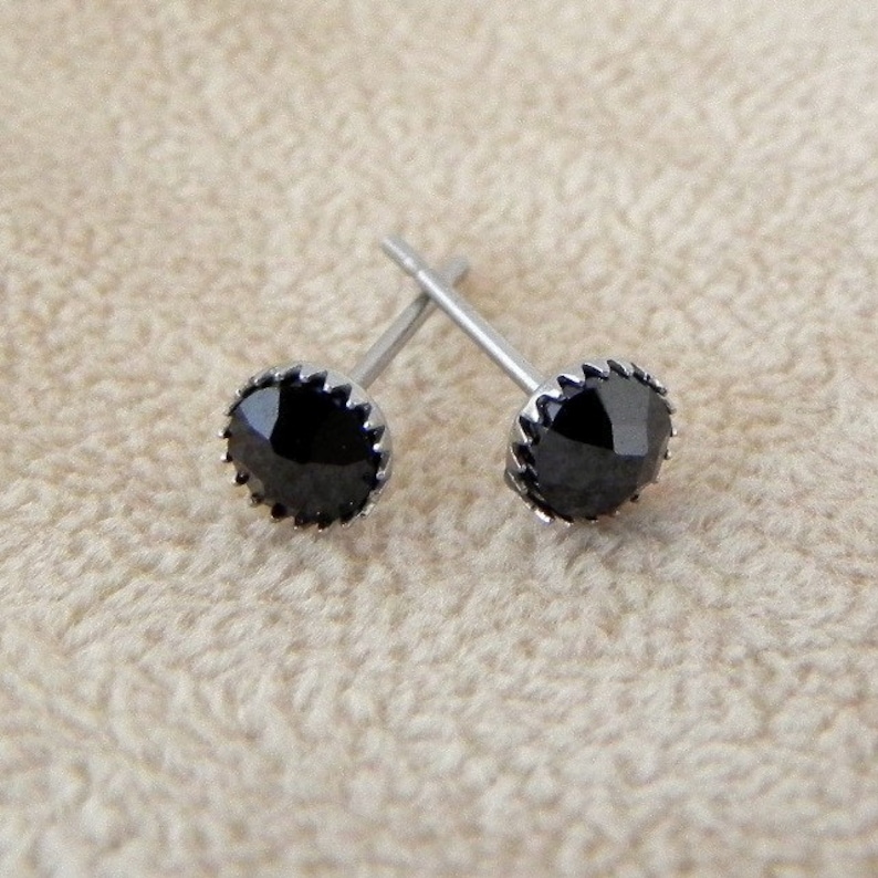May include: A pair of black stud earrings with a silver setting. The earrings have a round, faceted black stone in the center.