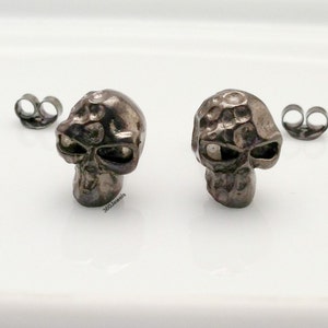 May include: A pair of silver skull stud earrings. The skulls are textured and have a slightly distressed look.