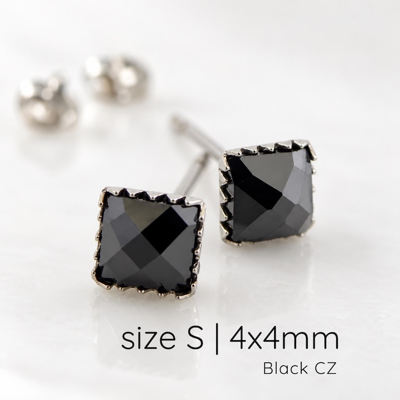Puede incluir: Un par de pendientes de bot&oacute;n cuadrados con piedras de circonita c&uacute;bica negra facetadas en un marco met&aacute;lico. El texto size S | 4x4mm Black CZ es visible. Cada pendiente tiene un poste y un cierre met&aacute;lico a juego incluido.